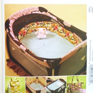 May include: A sewing pattern for home decorating, featuring a baby playard with a floral and pink trim, a light blue mesh base, and a small stuffed animal. The pattern includes images of coordinating accessories.