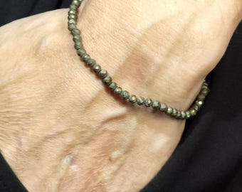 May include: A gold-toned beaded bracelet with a faceted finish. The bracelet is worn on a person's wrist.