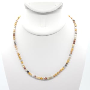 May include: A necklace made of small, round, multi-coloured stones. The stones are shades of brown, yellow, and white.
