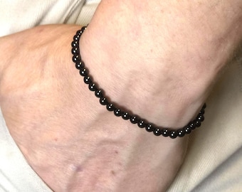 May include: A black beaded bracelet. The bracelet is made of small, round, black beads strung together. The bracelet is worn on the wrist.