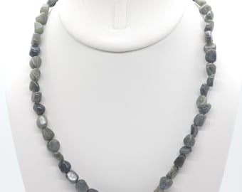 May include: A necklace composed of irregularly shaped, polished gray labradorite stones. The stones are strung together, creating a unique and natural look. The necklace is displayed on a white jewelry stand, showcasing its color variations and textures.