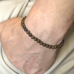 Puede incluir: Una pulsera de cuentas con pequeñas cuentas redondas de color marrón oscuro. Las cuentas tienen un ligero brillo. La pulsera se lleva en la muñeca. Un accesorio sencillo y elegante.