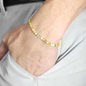 Op de afbeelding: Een armband gemaakt van kleine, ronde, gele en witte kralen. De armband zit om een pols.