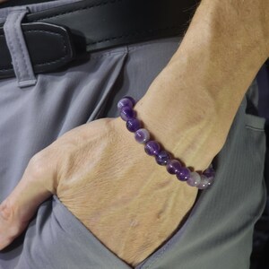 May include: A purple amethyst beaded bracelet on a person's wrist.