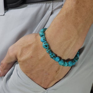 May include: A turquoise blue skull bead bracelet. The beads are round and have a skull design.