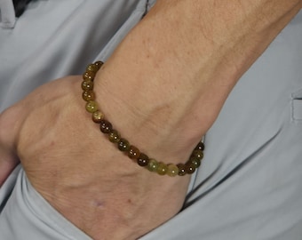 May include: A green and brown beaded bracelet on a person's wrist.