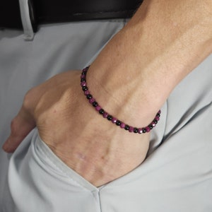 May include: A bracelet made of black and pink beads. The bracelet is on a person's wrist.