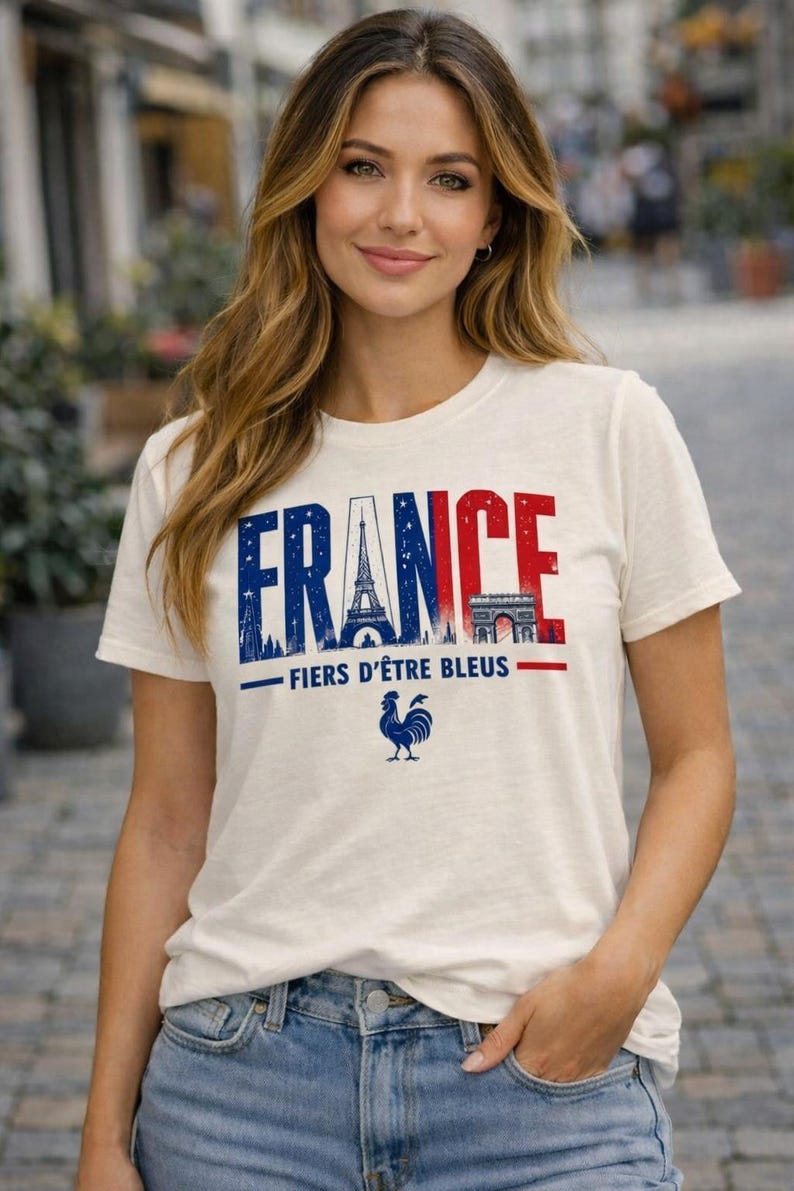 May include: Off-white t-shirt with the word "FRANCE" in blue and red, featuring the Eiffel Tower and Arc de Triomphe. Below, the text "FIERS D'&Ecirc;TRE BLEUS" and a blue rooster graphic. The shirt is worn by a person.