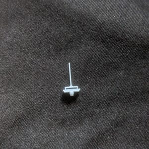 May include: A small, white plastic piece with a thin, vertical rod and a flat, rectangular base. The piece is designed to be used as a stand or support.