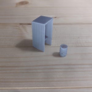 Pode incluir: Um modelo de um pequeno edifício impresso em 3D em plástico cinza com uma estrutura cilíndrica ao lado.