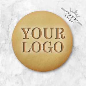 Op de afbeelding: Een lichtbruine koek met de tekst "YOUR LOGO" in reliëf op het oppervlak. De koek ligt op een witte marmeren achtergrond.