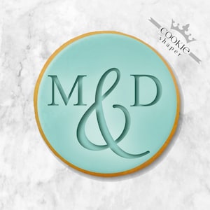 Peut inclure: Un emporte-pièce rond de couleur bleu clair avec un contour doré. L'emporte-pièce présente les lettres "M & D" en écriture cursive.