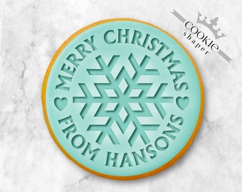 May include: A turquoise blue cookie cutter with a gold outline. The cutter is shaped like a circle with a snowflake design in the center. The text "Merry Christmas from Hansons" is written around the snowflake.