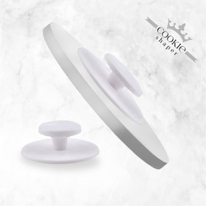 以下が含まれることがあります： 白いプラスチック製のクッキーシェイパーで、丸くて平らな取り外し可能なベースが2つ付いています。ベースの中央には、小さく丸い突起があります。シェイパーには「cookie shaper」と王冠のマークが付けられています。