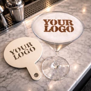May include: A martini glass with a foamy top featuring the words "YOUR LOGO" in brown. A matching white coaster with the same text sits beside the glass. The drink is on a marble surface.