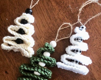 May include: Three handmade crochet Christmas tree ornaments. One is cream-colored with black beads, another is green with white beads, and the third is white with black and white checkered beads. Each has a jute twine loop for hanging.