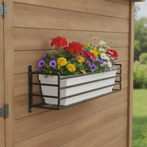 May include: A rectangular white plastic planter box held within a black metal frame mounted to a wooden wall. The planter is filled with a vibrant arrangement of red, yellow, purple, and white flowers with green foliage, creating a colourful display.