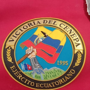 May include: A black and gold embroidered patch with the text "Victoria del Cenepa" and "Ejercito Ecuatoriano" surrounding a depiction of a hand holding the flag of Ecuador. The year 1995 is also embroidered on the patch.
