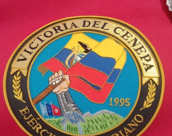 May include: A black and gold embroidered patch with the text "Victoria del Cenepa" and "Ejercito Ecuatoriano" surrounding a depiction of a hand holding the flag of Ecuador. The year 1995 is also embroidered on the patch.