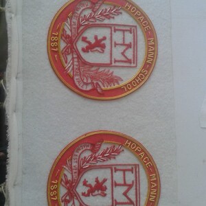 May include: Two red and gold embroidered patches with the text "Hopace-Mann-School" and "Magna Est Veritas Et Praevalet" around the edge. The center of each patch features a red lion and the letters "HM".