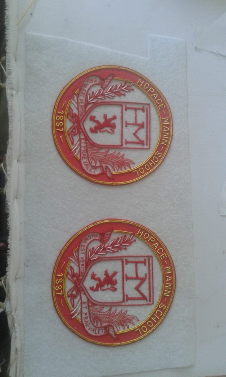 May include: Two red and gold embroidered patches with the text "Hopace-Mann-School" and "Magna Est Veritas Et Praevalet" around the edge. The center of each patch features a red lion and the letters "HM".