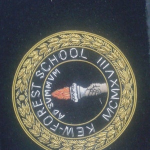 May include: A gold embroidered patch with a black background. The patch features a torch, a wreath of leaves, and the text "K.E.W.-FOREST SCHOOL MCMXXXVII".