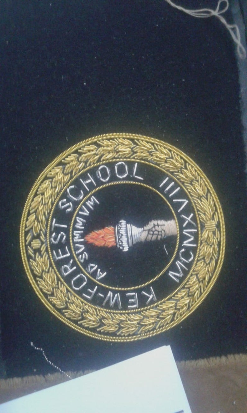 May include: A gold embroidered patch with a black background. The patch features a torch, a wreath of leaves, and the text "K.E.W.-FOREST SCHOOL MCMXXXVII".