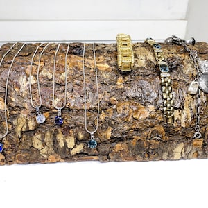 Può includere: Un espositore in legno con collane d'argento decorate con pietre preziose di vari colori, tra cui blu e trasparente. Ci sono anche braccialetti d'oro e una catena d'argento con un ciondolo sul tronco.