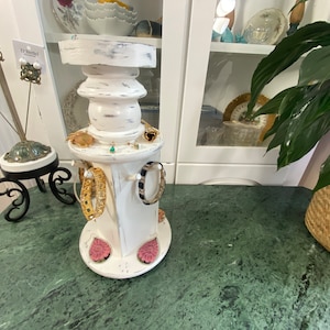 May include: White wooden jewelry organizer with a distressed finish. The organizer has a rotating base and multiple compartments for storing earrings, bracelets, and necklaces. The organizer is sitting on a green marble surface.
