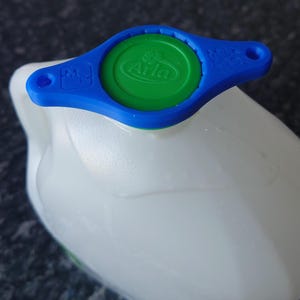 May include: A blue and green plastic milk jug lid with a green circle and the word "Arla" in white lettering. The lid has a blue handle with a small hole in the top.