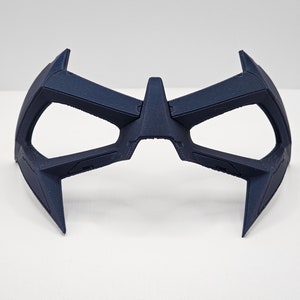 May include: A dark blue plastic mask with a geometric design. The mask has two eye holes and a pointed top.
