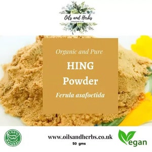 May include: A close-up of a pile of organic and pure hing powder, a yellow-brown spice, in a white bowl. The powder is labelled "Organic and Pure HING Powder Ferula asafoetida" and is 50 grams. The image also includes a green logo with the text "100% NATURAL" and a green logo with the text "vegan".