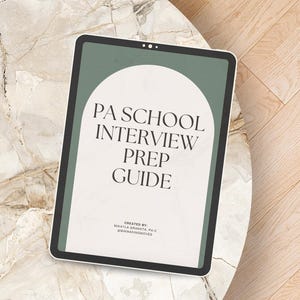 May include: A digital tablet displaying the text "PA SCHOOL INTERVIEW PREP GUIDE" in a modern font. The tablet has a green border and a white background with an arched design. The tablet rests on a marble-patterned table.