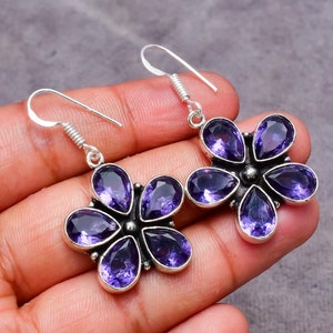 May include: A pair of silver flower-shaped earrings with purple amethyst gemstones. The earrings have a simple hook closure.