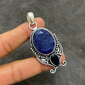 May include: A silver pendant featuring a large oval blue sapphire gemstone and a smaller pear-shaped blue sapphire gemstone. The pendant has an intricate silver design.