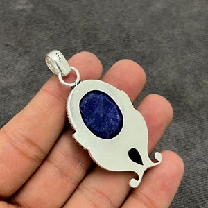 Op de afbeelding: Zilveren hanger met een blauwe edelsteen in een decoratief frame. De hanger heeft een lus met het nummer 925 erop.