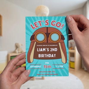 Puede incluir: Una invitaci&oacute;n de cumplea&ntilde;os con un fondo turquesa y una ilustraci&oacute;n de casco de aviador retro. El texto "LET'S GO!" est&aacute; en la parte superior, con "LIAM'S 2ND BIRTHDAY" en el centro. La fecha y la hora tambi&eacute;n est&aacute;n incluidas.