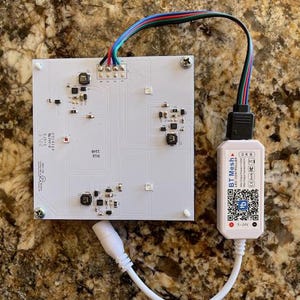 May include: A white circuit board with a black connector and a white wire. The circuit board has a black screw in the top right corner. The connector is labeled "BT Mesh LED Controller".