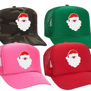 May include: Four trucker hats featuring a Santa Claus design. The hats are in camouflage, green, pink and red.
