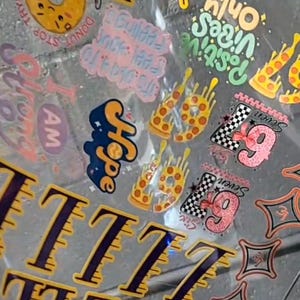 Peut inclure: Une collection d'autocollants colorés avec divers motifs. Comprend un donut souriant, le mot "Hope", des tranches de pizza et la phrase "Positive Vibes Only". Comprend également le chiffre "7" et d'autres graphiques.