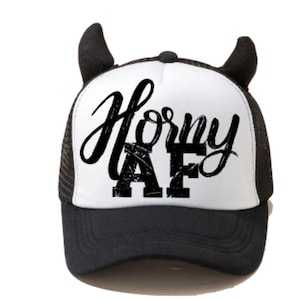 May include: A black and white trucker hat with devil horns. The hat has a white front with black mesh on the back and sides. The front of the hat has the text "Horny AF" in black.