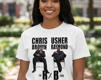May include: White t-shirt featuring the text "CHRIS BROWN USHER RAYMOND" above images of the artists. Below the images is "THE R&B TOUR RAYMOND & BROWN" in black text. The shirt is worn by a person.