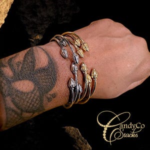 May include: A set of four gold and silver bangle bracelets with decorative acorn-shaped ends. The bracelets are stacked on a person's wrist.