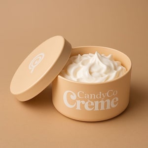 Puede incluir: Un recipiente de color melocotón claro con una tapa a juego, lleno de crema batida blanca. El recipiente tiene las palabras "CandyCo Crème" en escritura blanca. La tapa está ligeramente entreabierta, revelando el contenido cremoso.