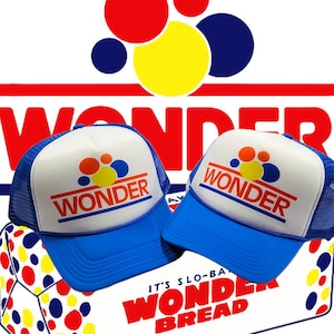 Puede incluir: Dos gorras de camionero azules y blancas con el logotipo de Wonder Bread y una caja de Wonder Bread con el lema "It's Slo-Baked Wonder Bread".