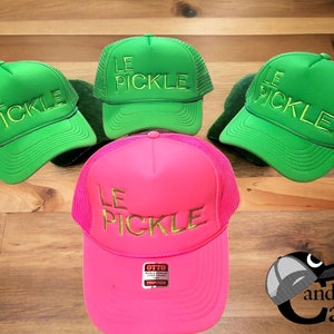 Könnte beinhalten: Drei Trucker-Caps mit dem Schriftzug "Le Pickle" in goldener Stickerei. Eine Mütze ist pink, zwei sind grün.