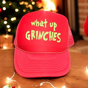May include: Red trucker hat with a green embroidered design that says "what up GRINCHES".