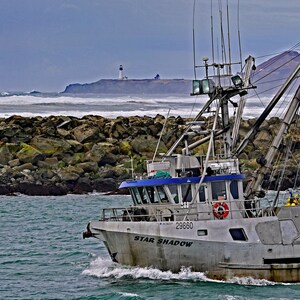 May include: A gray fishing boat, the "Star Shadow", navigates choppy ocean waters. The boat has a blue cabin top and a large crane. A lighthouse sits on a distant rocky shore under a cloudy sky.