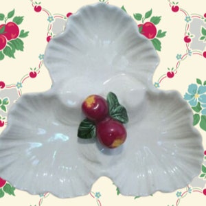 Könnte beinhalten: Eine weiße Keramik-Servierplatte in Form von drei überlappenden Blättern mit einem erhabenen Design aus roten Äpfeln und grünen Blättern.