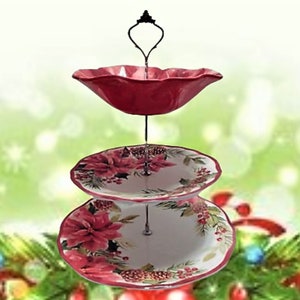 May include: A three-tiered serving stand with a red, white and green floral design. The top tier is a red bowl with a scalloped edge. The bottom two tiers are white plates with a scalloped edge and a floral design featuring poinsettias, pine branches and berries.